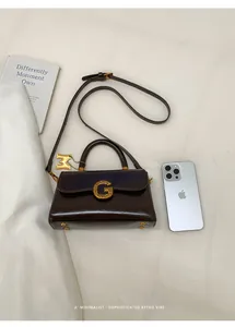 Close-up of brown leather handbag with gold metal logo and strap on neutral background