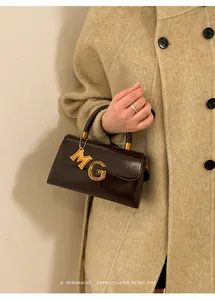 Detail of dark brown leather handbag featuring a signature gold metal MG pendant