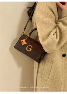 Detail of retro matte brown shoulder bag with gold G logo buckle on tweed coat
