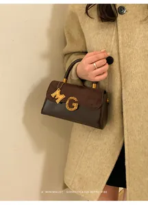Close-up of retro brown matte leather handbag with gold metal G logo and wooden handle