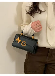 Detail of black vintage handbag with textured golden G-lock and orange M-charm pendant