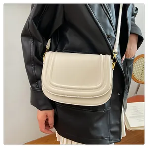 Détail d'un sac besace beige avec des coutures incurvées et des boucles en métal doré