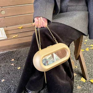 Sac à chaîne capsule doré mat avec miroir ovale sur fond extérieur de feuilles de ginkgo