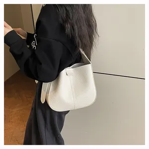 Gros plan d'un sac seau en cuir grainé blanc porté à l'épaule sur un pull-over noir décontracté