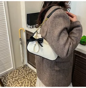 Dettaglio della borsa in pelle bianca con fiocco nero, ciondolo di perle e catena d'oro