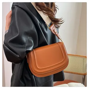 Détail d'un sac besace marron avec rabat en U et bandoulière large en tissu bicolore
