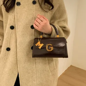 Retro dark brown glossy leather handbag with gold G-buckle and M-pendant details