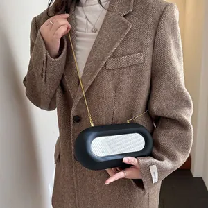 Sac bandoulière noir mat moderne avec chaîne dorée et miroir ovale sur un costume