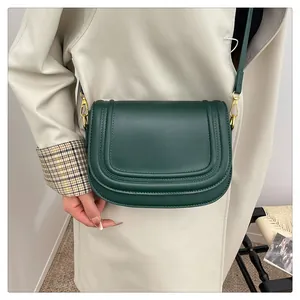 Vue détaillée du sac besace vert foncé avec triple couture sur un trench-coat beige