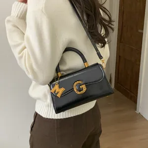 Glossy black leather shoulder bag with gold G-buckle and M-pendant on a model