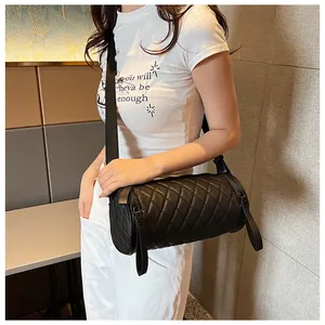 Detailed close-up of black quilted cylinder crossbody bag with woven shoulder strap