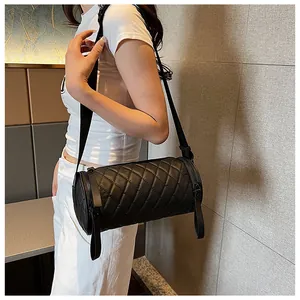 Side view of black quilted cylinder crossbody bag featuring wide fabric shoulder strap