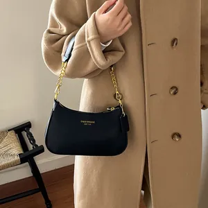 Elegante borsa a spalla nera con motivo litchi indossata con un cappotto color cammello
