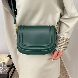 Sacoche selle classique en cuir vert foncé avec large bandoulière et trench beige