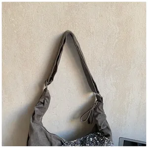 Detail of grey suede crescent bag featuring silver sequins and a wide shoulder strap