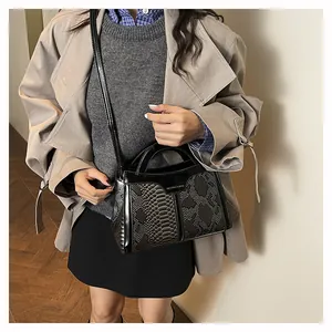Detail of black snake-embossed PU leather handbag with metal fashion logo plate