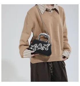 Detalle de elegante bolso de mano negro con cristales florales y asa metálica