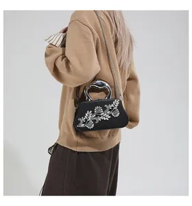 Detalle de bolso de noche negro con flores de strass plateadas y asa de corazón