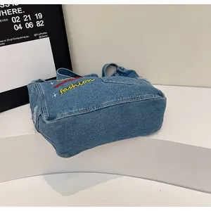 Detail of vintage denim bag featuring colorful embroidery and frayed pocket edges