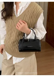 Détail du sac cylindrique noir brillant avec logo MUHETI et chaîne en métal argenté