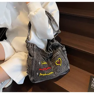 Detail of dark gray washed denim crossbody bag featuring heart and letter embroidery