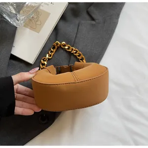 Détail d'un mini sac croissant marron avec chaîne dorée épaisse sur un magazine chic