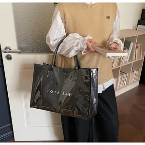 Glossy black tote bag with white TOTE BAG text shown being carried by a model