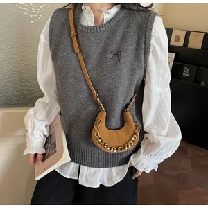 Sac croissant marron avec chaîne dorée porté sur un gilet en maille grise
