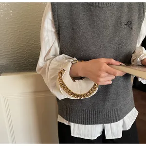 Détail d'un sac demi-lune beige avec chaîne dorée épaisse porté par un mannequin