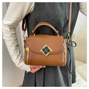 Détail du sac à main marron en cuir grainé avec fermoir géométrique doré et zips latéraux