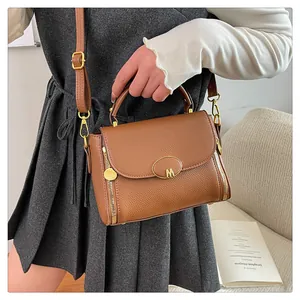 Détail d'un sac à main marron en cuir grainé avec logo M doré et fermetures éclair latérales
