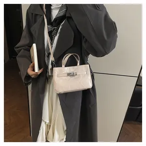 Vue détaillée d'un sac à main crème texturé avec fermoir argenté sur un manteau chic