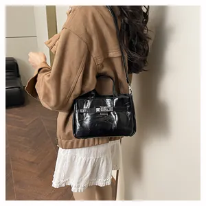Détail d'un sac à main noir brillant avec fermoir rotatif en métal et bandoulière fine