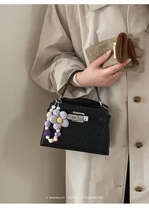 Detail of black crocodile-pattern handbag with purple crochet flower charm accessory