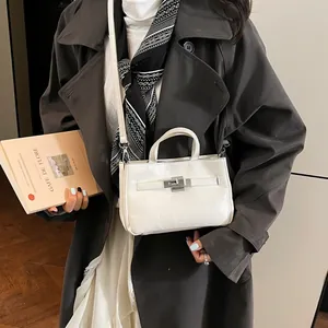 Sac à main blanc en cuir verni texturé avec fermoir argenté porté avec un trench-coat