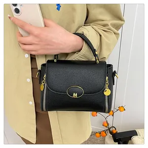 Détail du cuir grainé litchi sur sac à main noir avec logo M doré et zip décoratif
