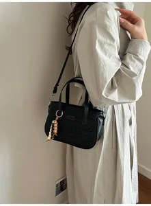 Gros plan du motif matelassé d'ours noir et du pompon en perles sur le sac