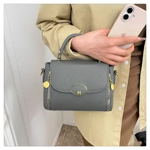 Détail du sac bandoulière gris texturé litchi avec logo M doré et zips décoratifs