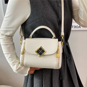 Sac à main blanc à motif litchi avec détails dorés porté par un mannequin en studio