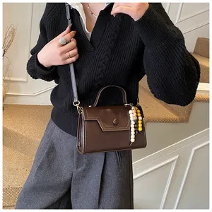 Detail view of deep brown vintage handbag featuring asymmetric flap and bead pendant