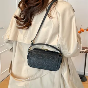Sac bandoulière pailleté noir avec poignée porté sur un trench-coat beige très élégant