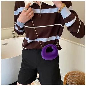 Detail of a purple velvet mini knot bag with a gold chain strap on a striped polo shirt
