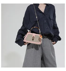 Close-up of woven straw handbag with pink leather trim and silk scarf handle detail