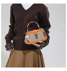 Detailed shot of beige straw woven handbag with orange leather trim and scarf handle