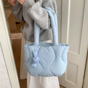Light blue quilted puffer tote bag with ribbon charm shown on shoulder for casual style