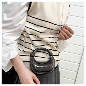 Détail d'un mini sac demi-lune fini brillant avec chaîne dorée porté par un mannequin