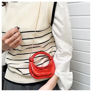 Détail du mini sac croissant rouge avec chaîne dorée et finition métallisée sur modèle