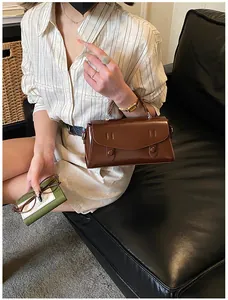 Brown vintage satchel bag with flap cover and button detail on a leather sofa