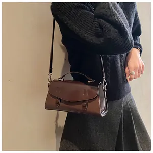 Detail of dark brown leather satchel with flap and double buckle shown on shoulder
