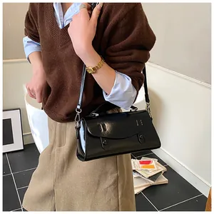 Close-up of a black patent leather satchel bag with metallic buckles and thin strap